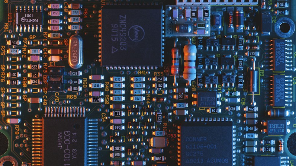 Close-up of blue printed circuit board showing the evolution from large discrete components to dense integrated circuits